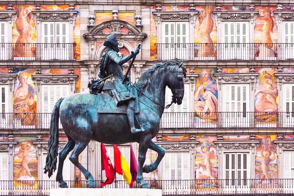 The bronze equestrian statue in front of the painted façades of Plaza Mayor
