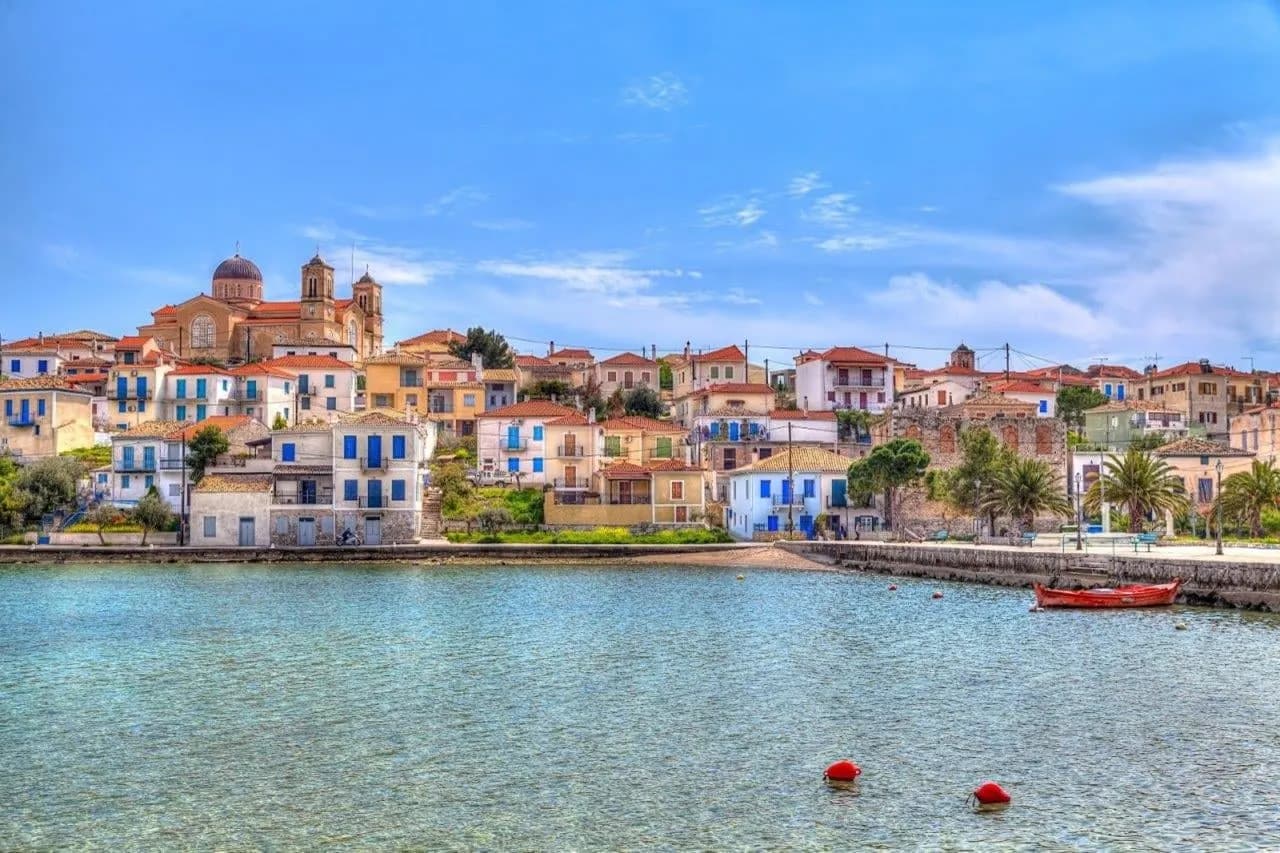 Colourful houses and a domed church along a calm Greek harbour