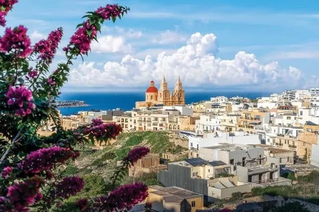 A hillside town with a red-domed church and the sea beyond, framed by bougainvillea
