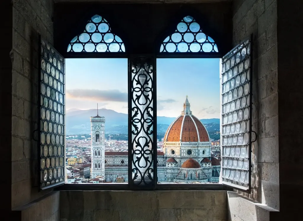 Florence Cathedral and its bell tower framed by an open Gothic window