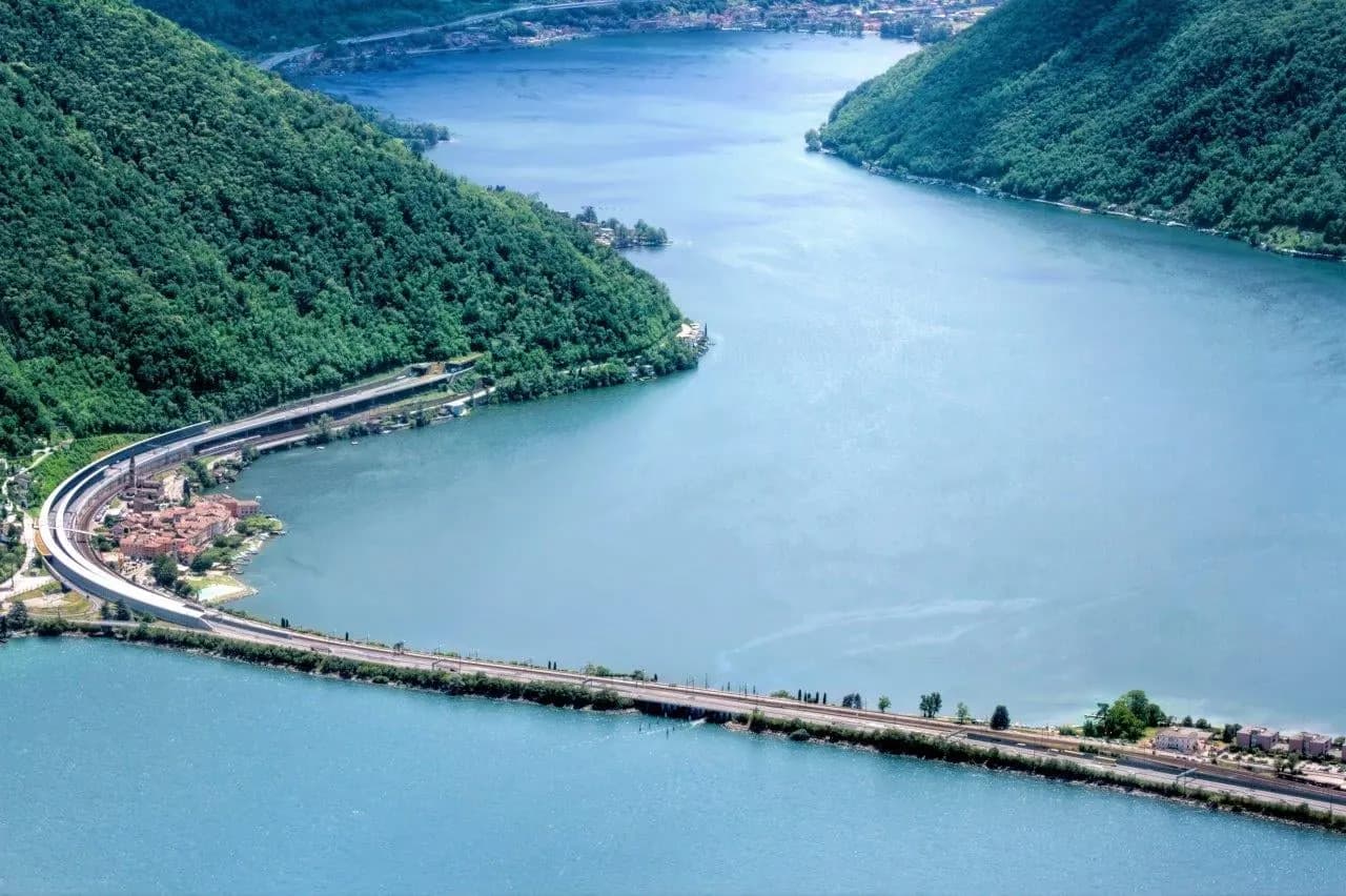 A causeway crossing Lake Lugano between forested slopes