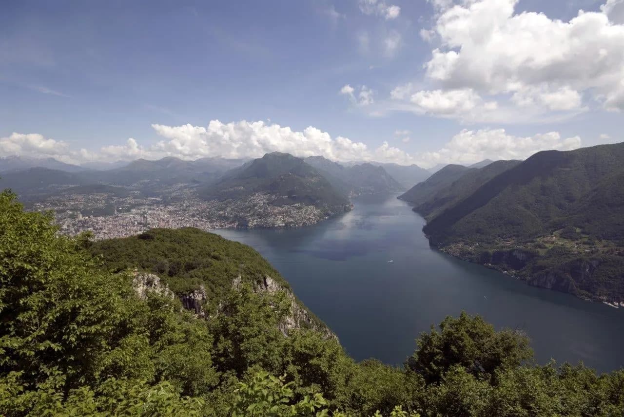 Lake Lugano winding between wooded mountains under a cloudy sky