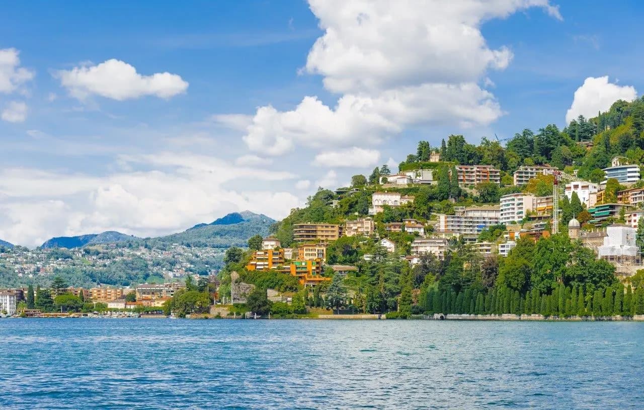 A lakeside town climbing a green hillside above blue water