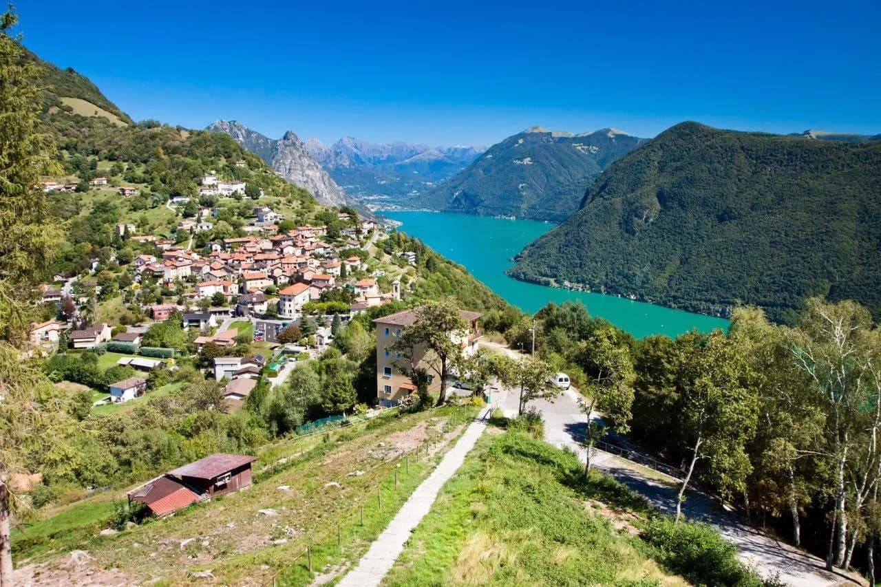 A hillside village above a turquoise lake with mountains beyond