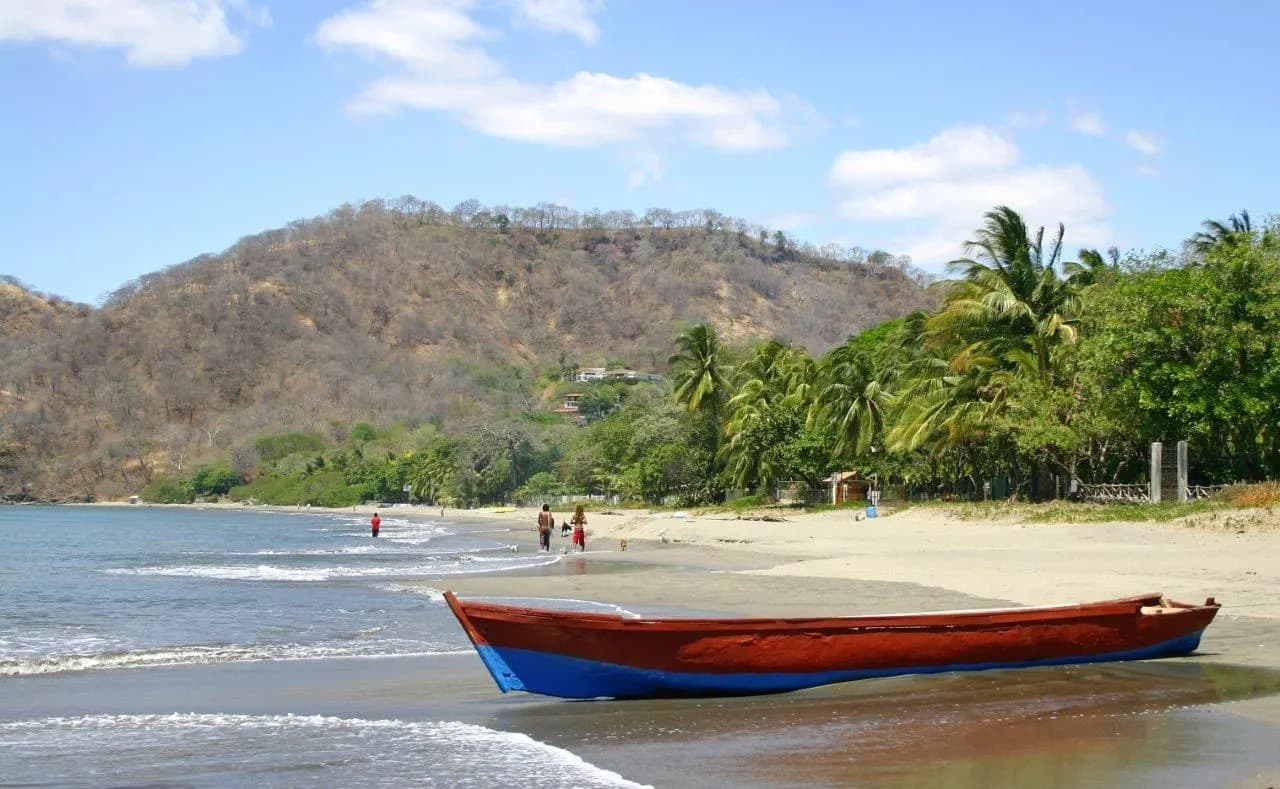 A wooden fishing boat drawn up on a palm-lined beach below green hills