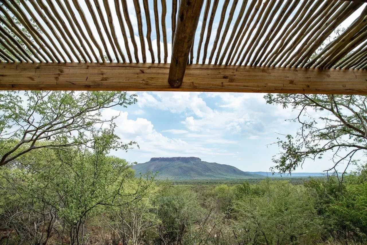 The view from a shaded lodge deck over green bush to a flat-topped mountain
