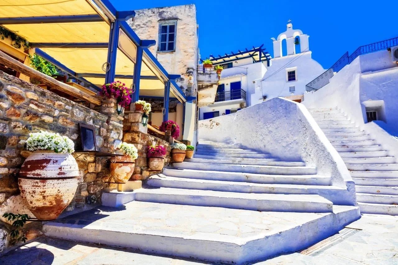 Whitewashed steps with blue railings and potted flowers below a chapel