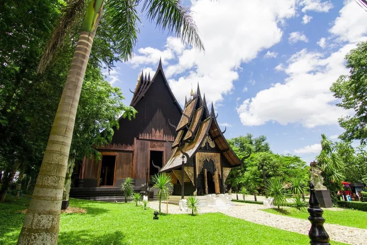 Dark wooden Lanna houses among palms and lawns at Baan Dam