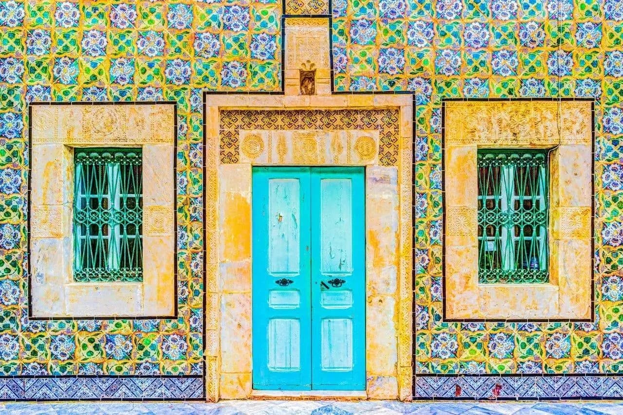 A turquoise door set in a wall of patterned Tunisian tiles