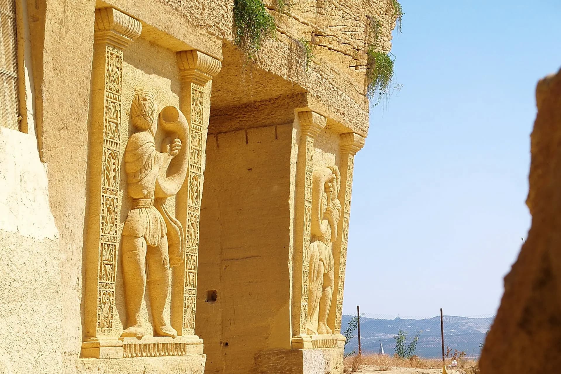 Tall figures carved into a sandstone rock face against a blue sky