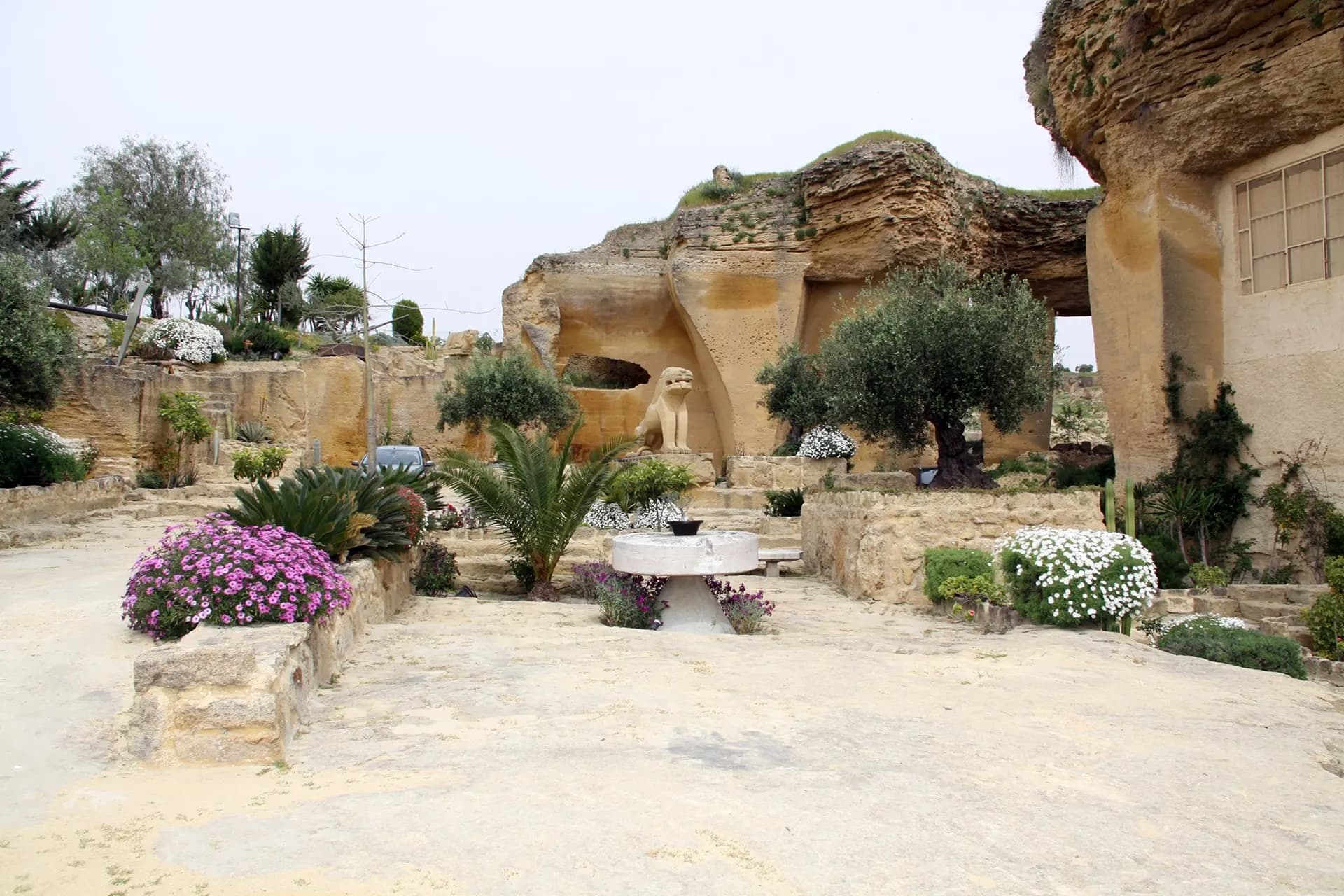 Flower beds and olive trees beneath the cut rock faces of the old quarry