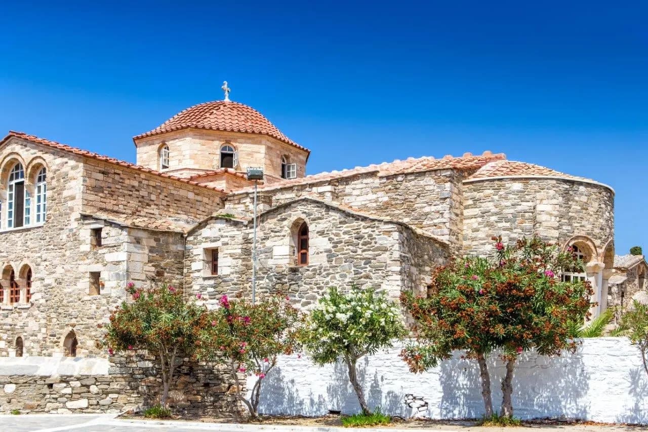 A Byzantine stone church with a tiled dome behind a whitewashed wall