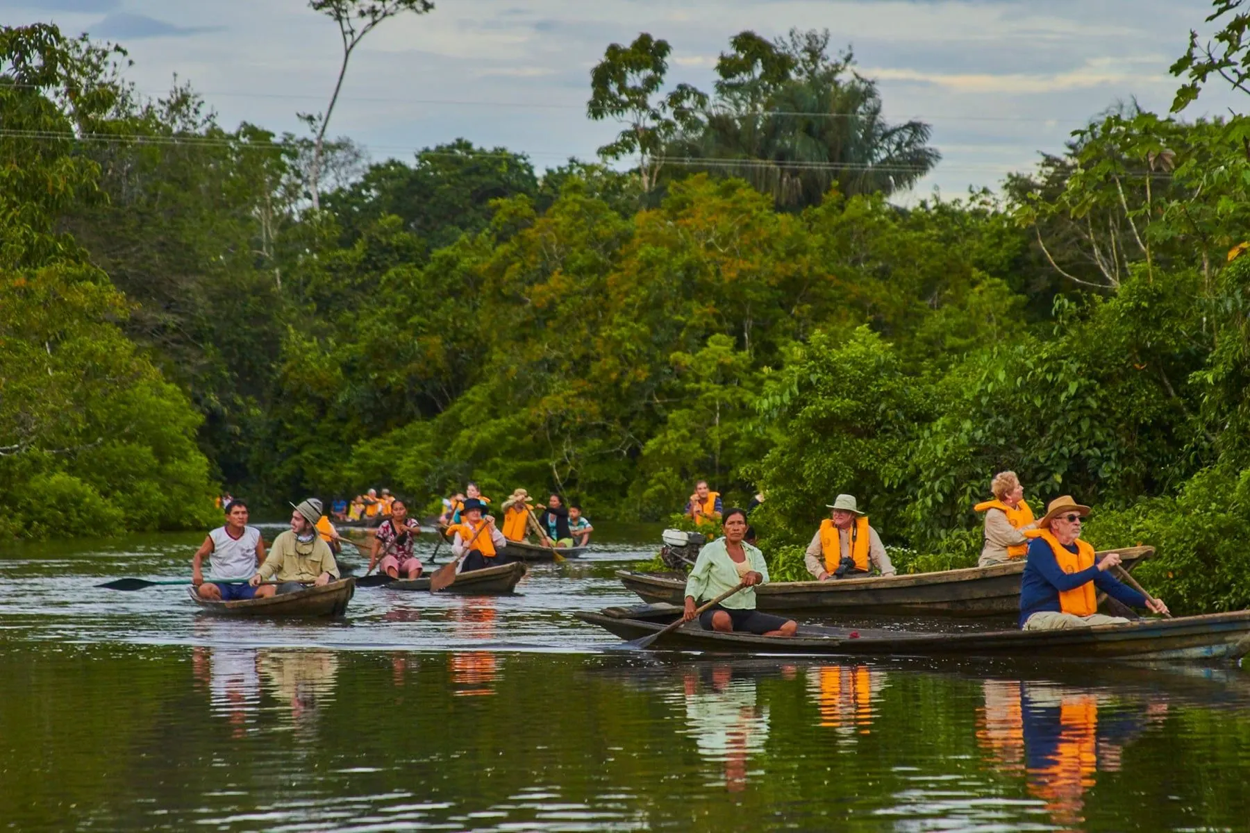 Small wooden canoes paddling along a calm rainforest creek
