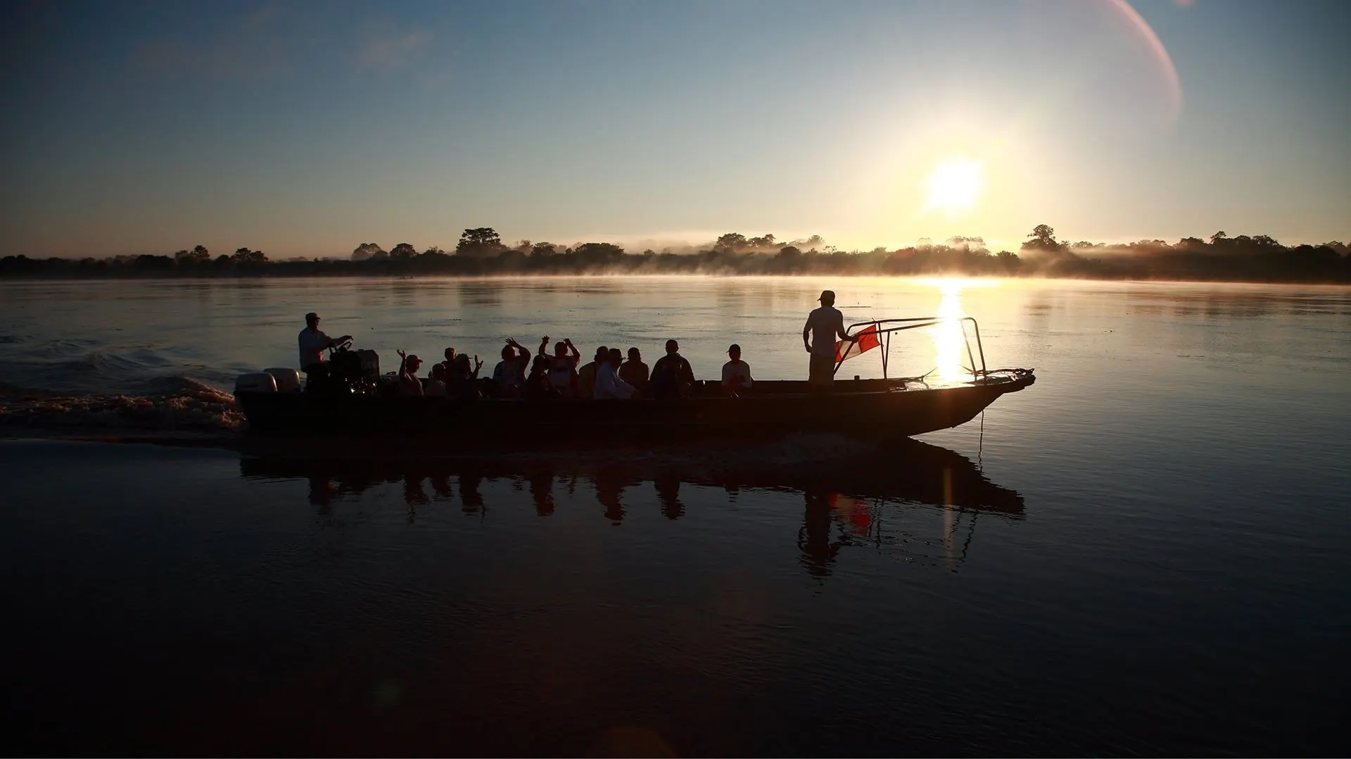 A skiff of travellers silhouetted on the river at sunrise