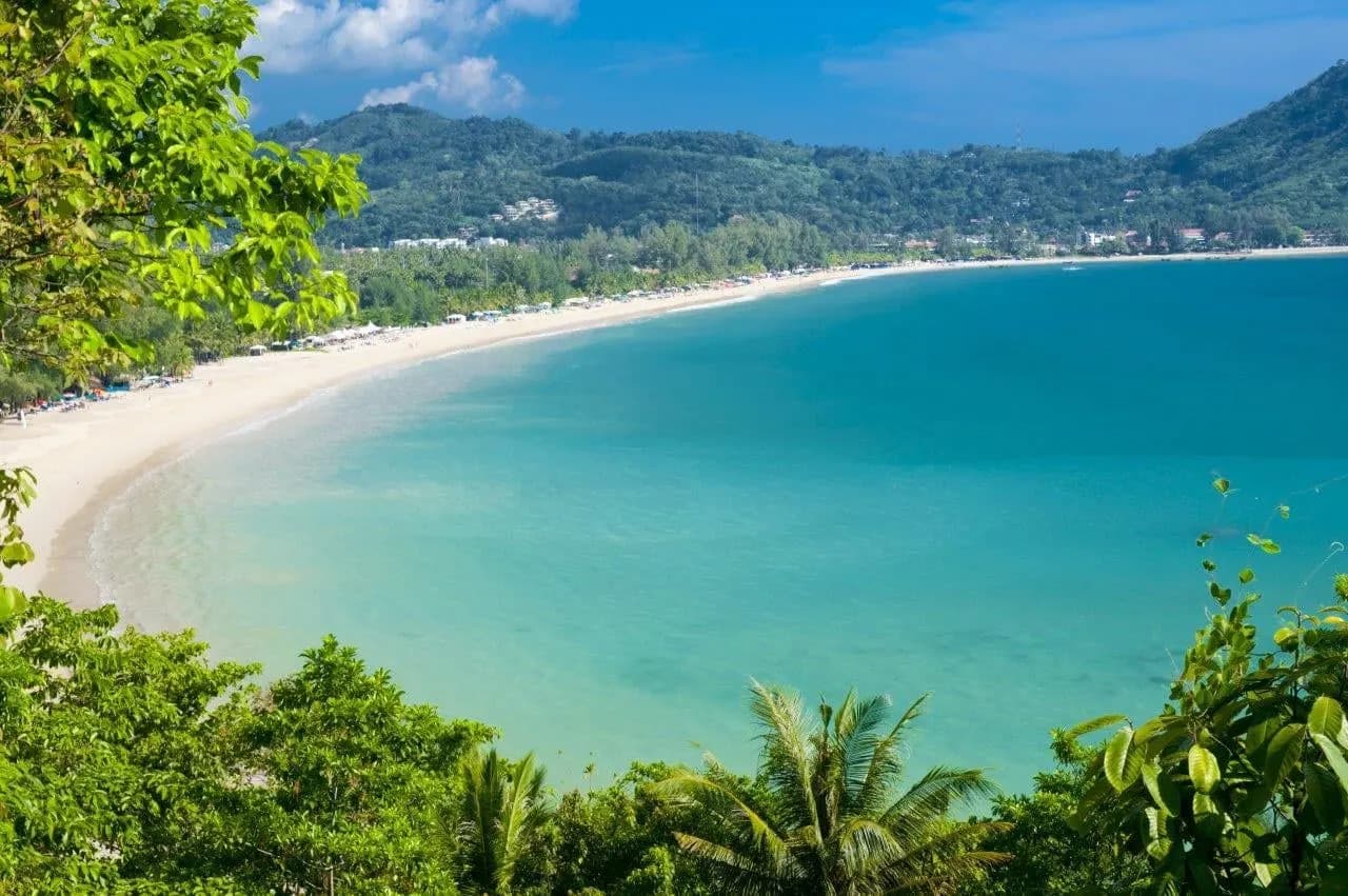 A long curving bay of turquoise water seen through jungle from a viewpoint