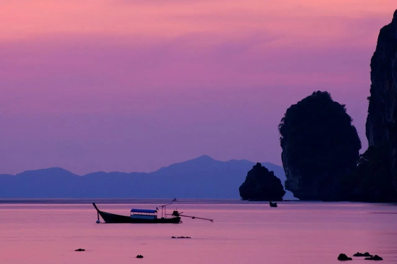A long-tail boat on a pink sunset sea beside limestone islets