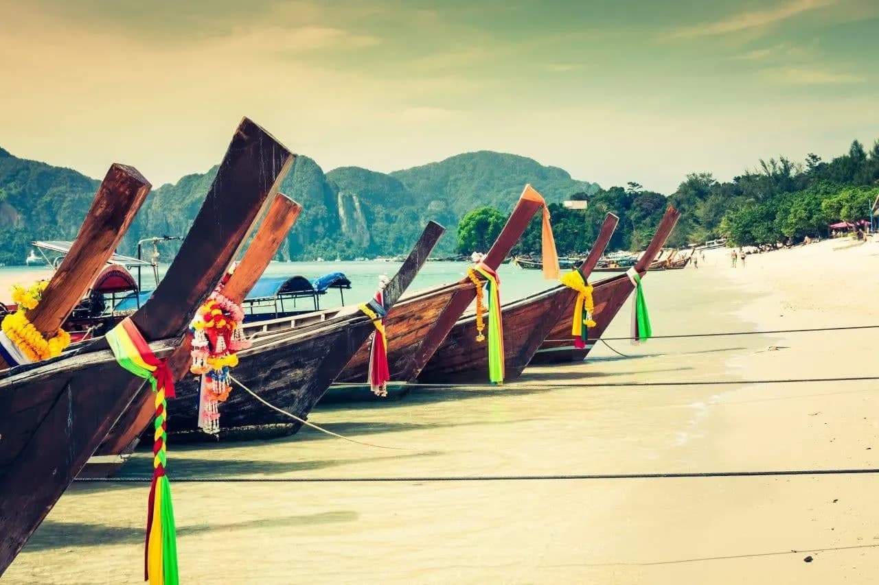 A line of wooden long-tail boats resting on a sandy beach with green hills behind