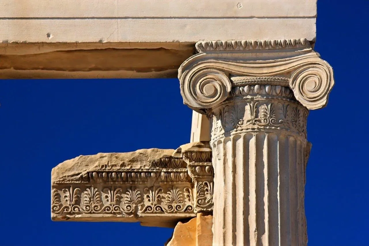 A carved Ionic capital and frieze against a deep blue sky