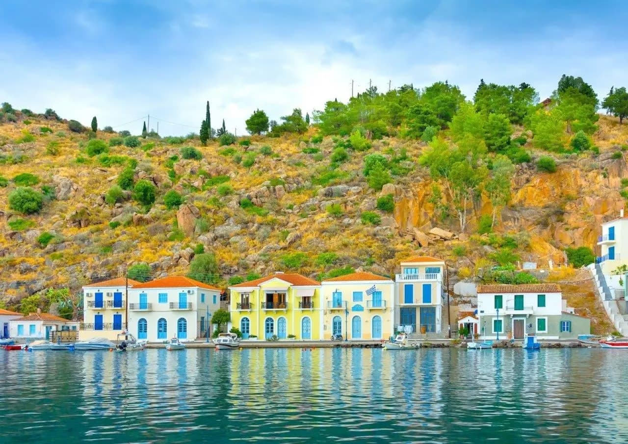Pastel houses along a calm harbour, below a green hillside