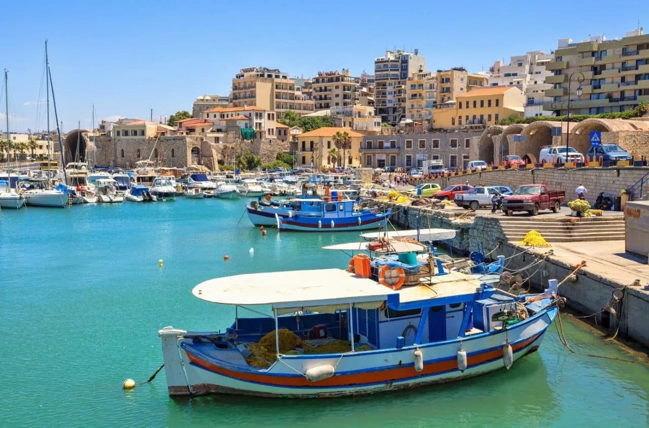 A blue and white fishing boat in Heraklion harbour, with the town behind