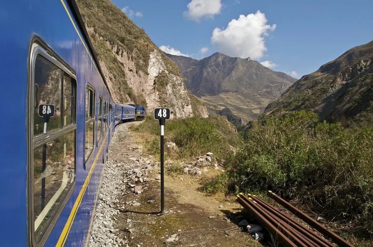 A blue train running through a mountain valley towards Machu Picchu