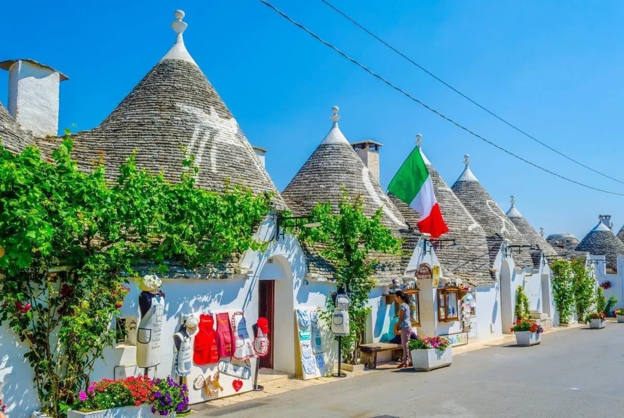 A street of white trulli with conical stone roofs and an Italian flag in Alberobello