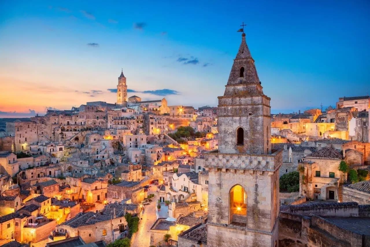 The old cave town of Matera lit up at dusk beneath a church bell tower