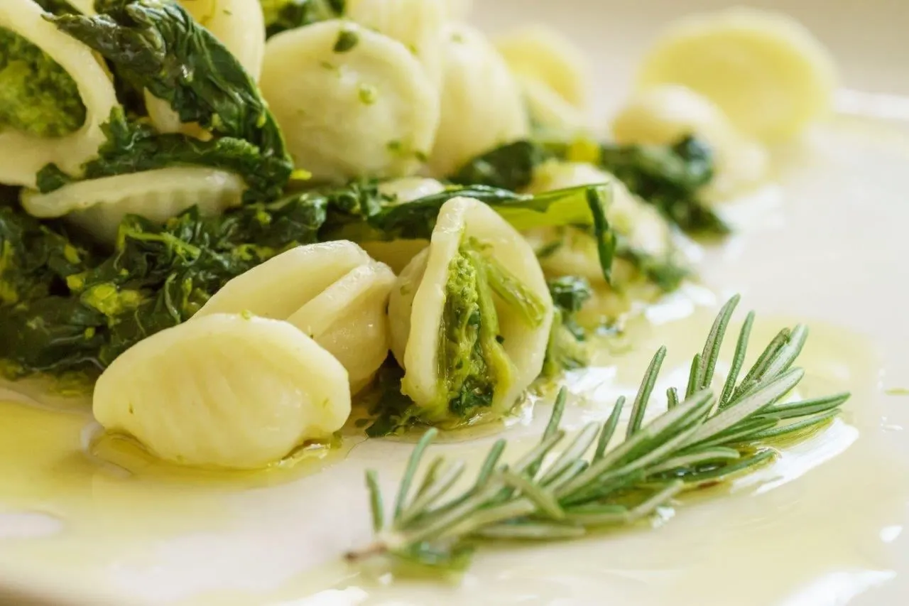 A plate of orecchiette pasta with greens, olive oil and a sprig of rosemary