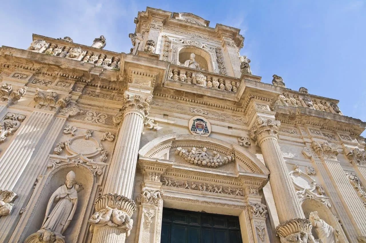 The carved stone baroque facade of a church in Lecce against a blue sky