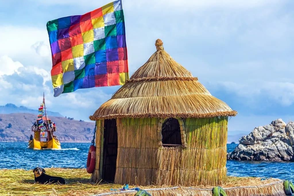 A reed hut and a rainbow flag on an Uros island, with a reed boat beyond