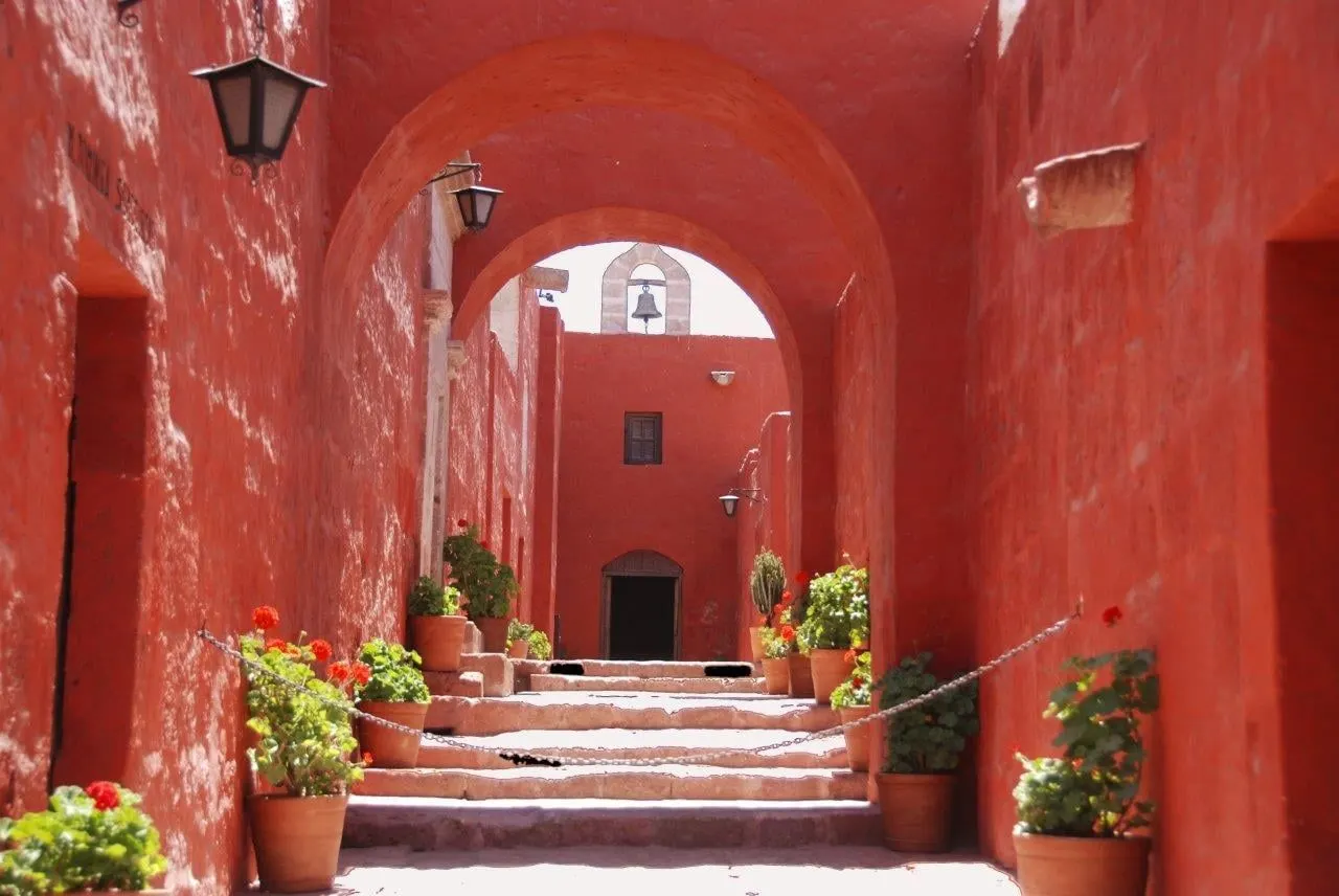 A red-walled lane with arches and potted geraniums in the Monastery of Santa Catalina