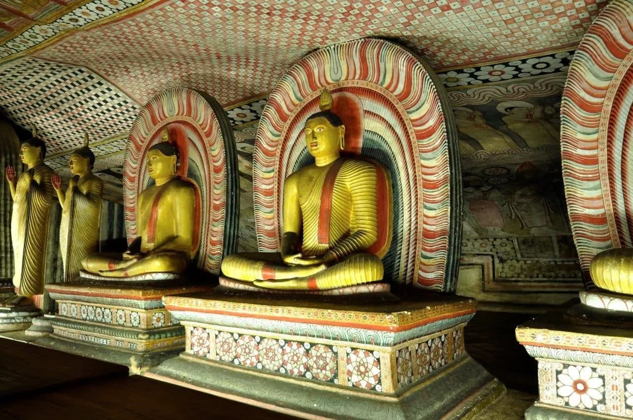 Rows of seated golden Buddha statues beneath painted arches in a cave temple