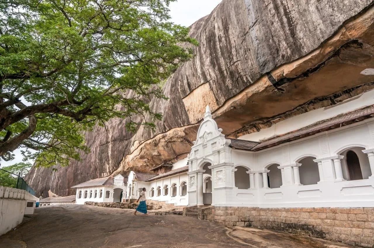 A white colonnaded temple front built under a huge rock overhang