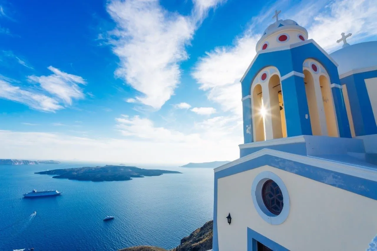 A blue and white bell tower against the sky above the sea
