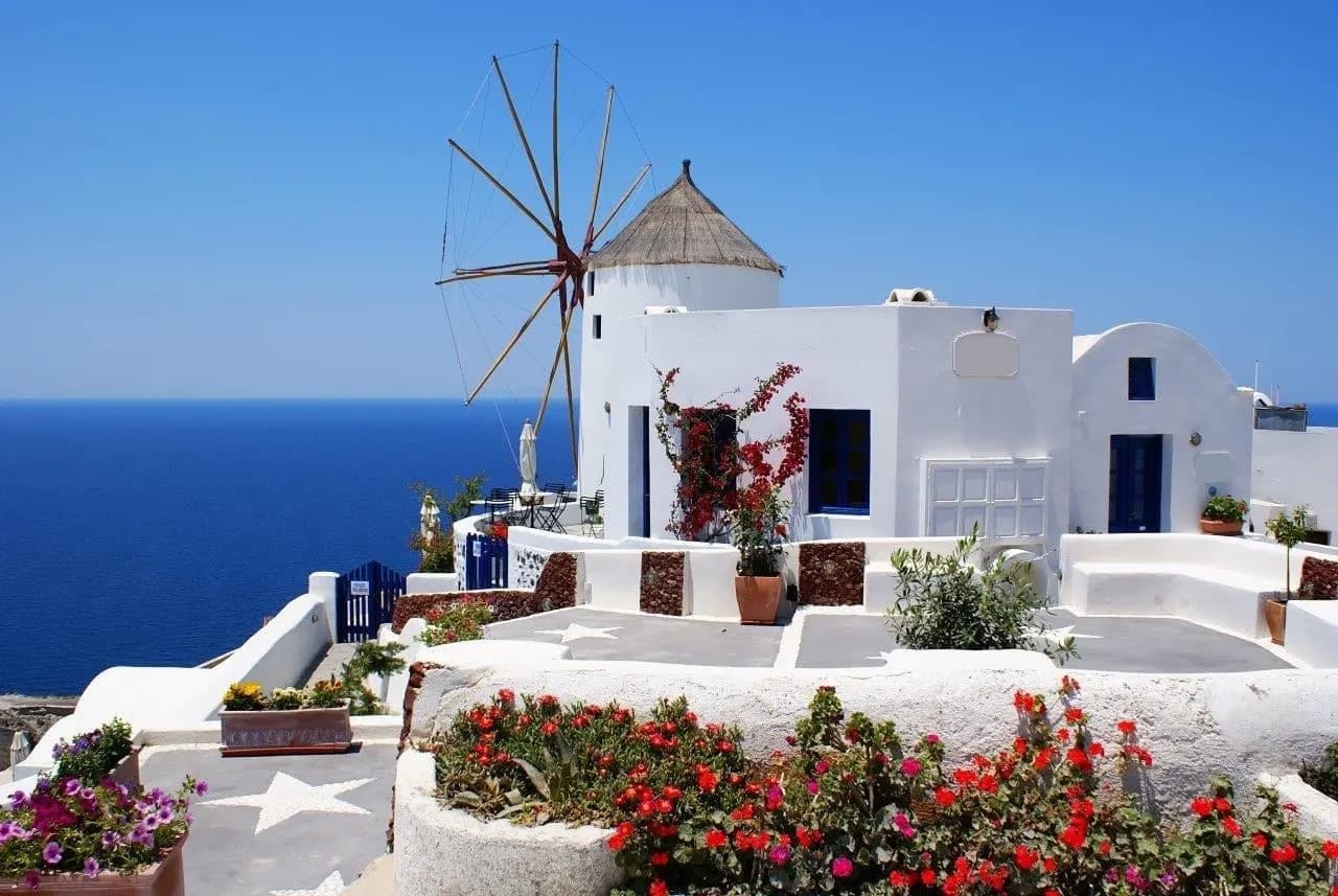 A white windmill above a terrace of red flowers and the sea