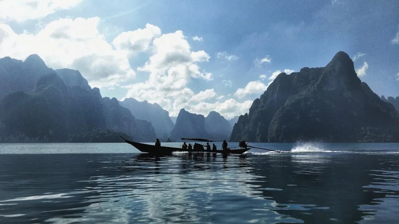 A longtail boat crossing Cheow Lan Lake beneath limestone peaks