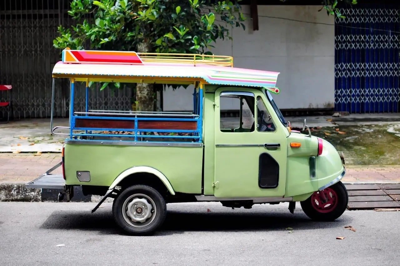 A pale green three-wheeled tuk-tuk parked on a southern Thai street