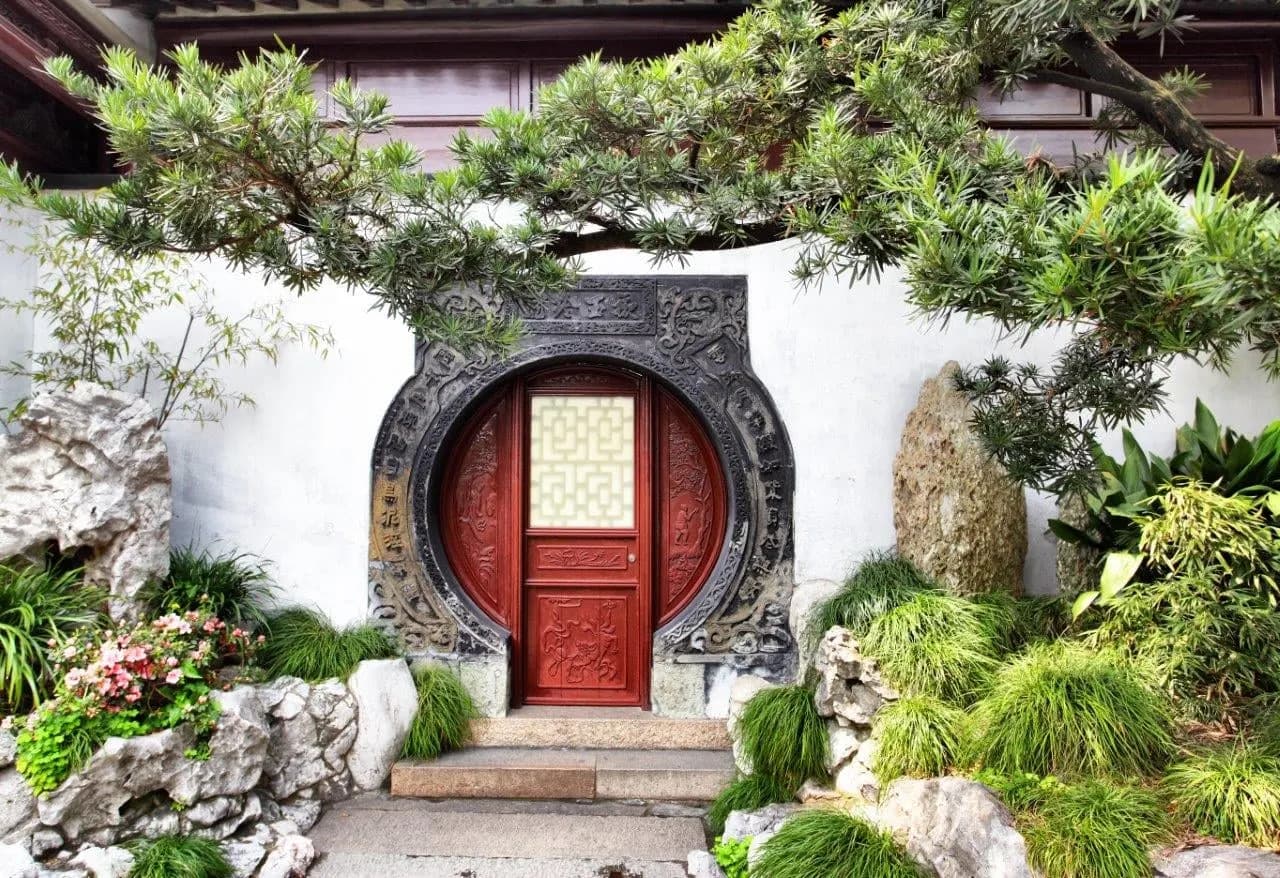 A round moon gate with a red door among pines and rockery