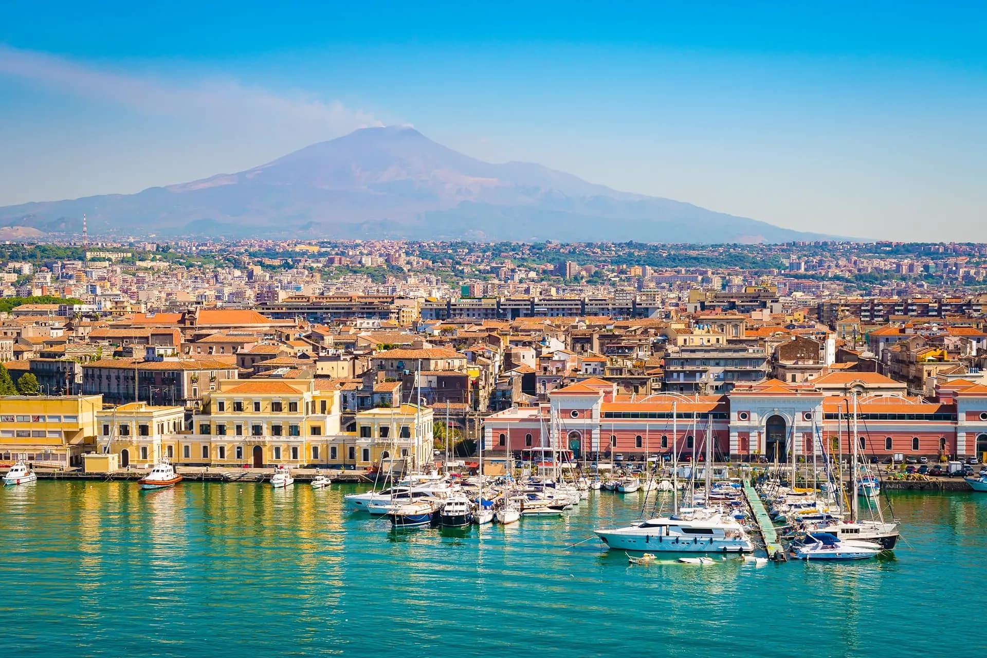 Boats in Catania harbour with Mount Etna rising behind the city