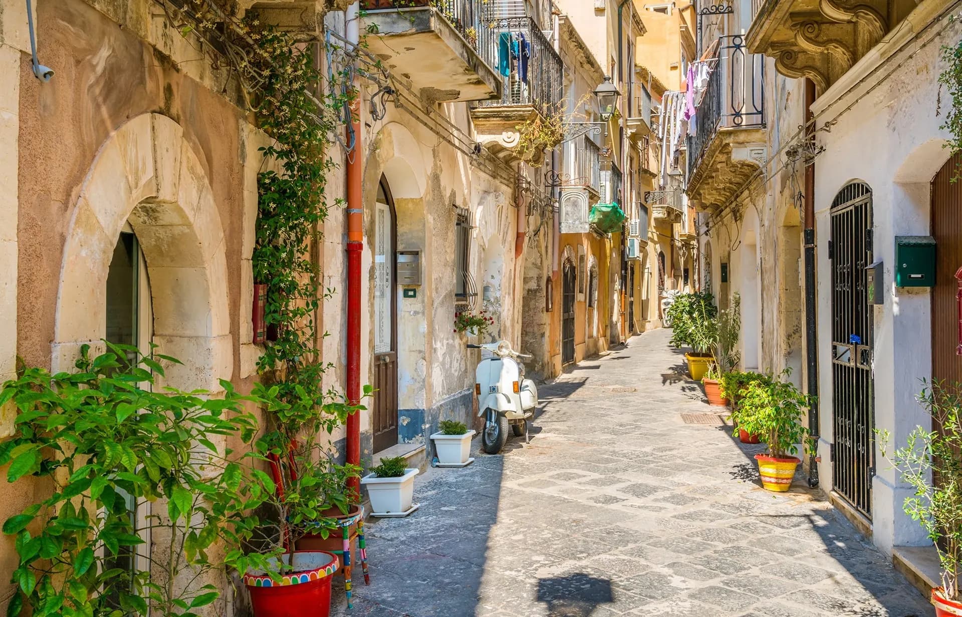 A narrow paved lane with potted plants and balconies in a Sicilian old town