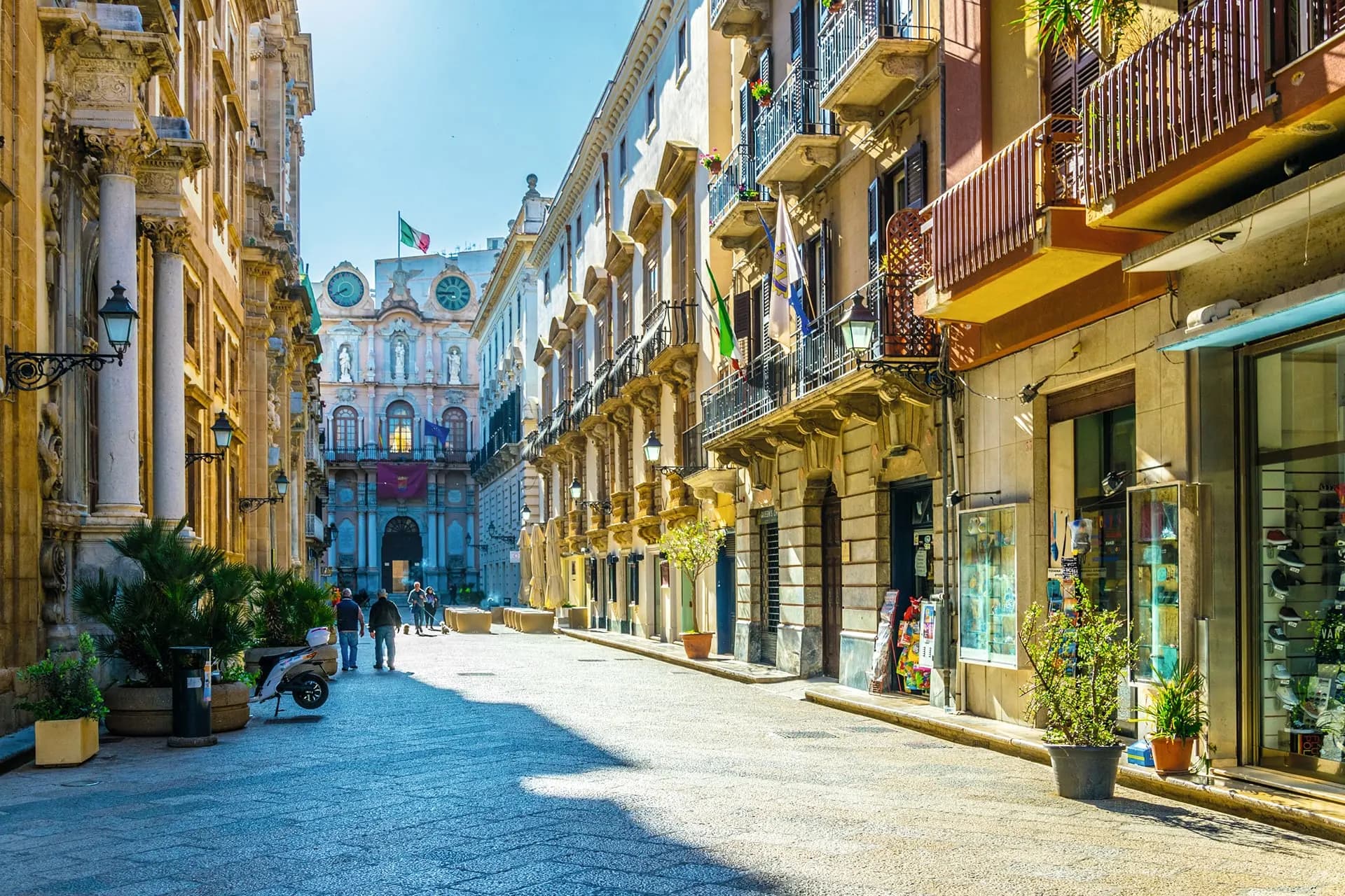 A sunlit pedestrian street lined with baroque palaces and balconies in an old Sicilian town
