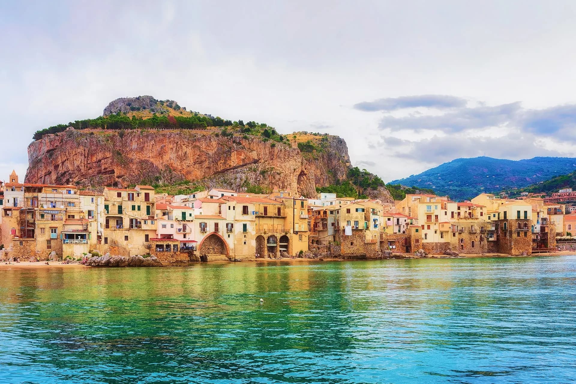 The waterfront houses of Cefalù beneath its rock, over clear green water