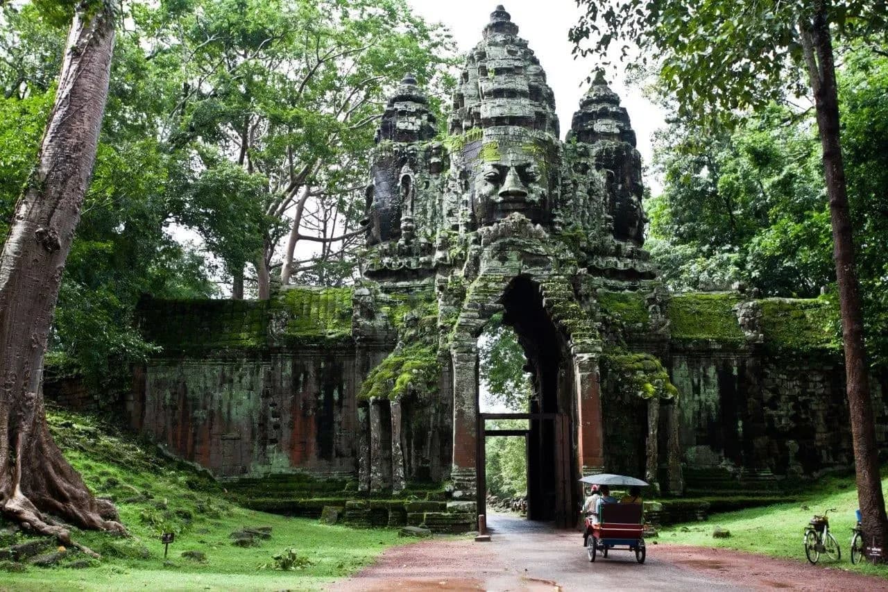 A face tower over a forest gateway, with a tuk-tuk passing through