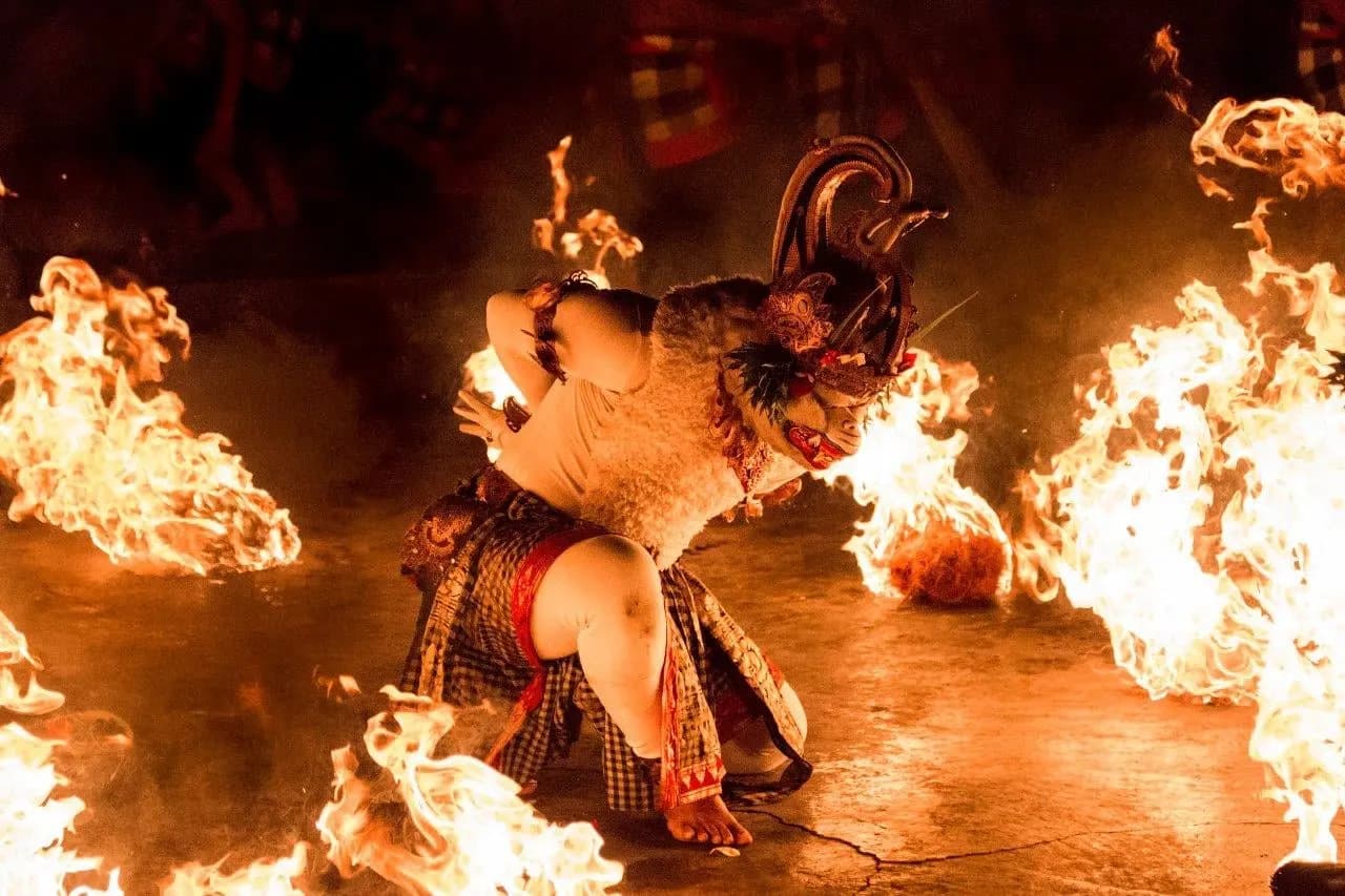 A masked dancer crouching between flames during an evening fire dance