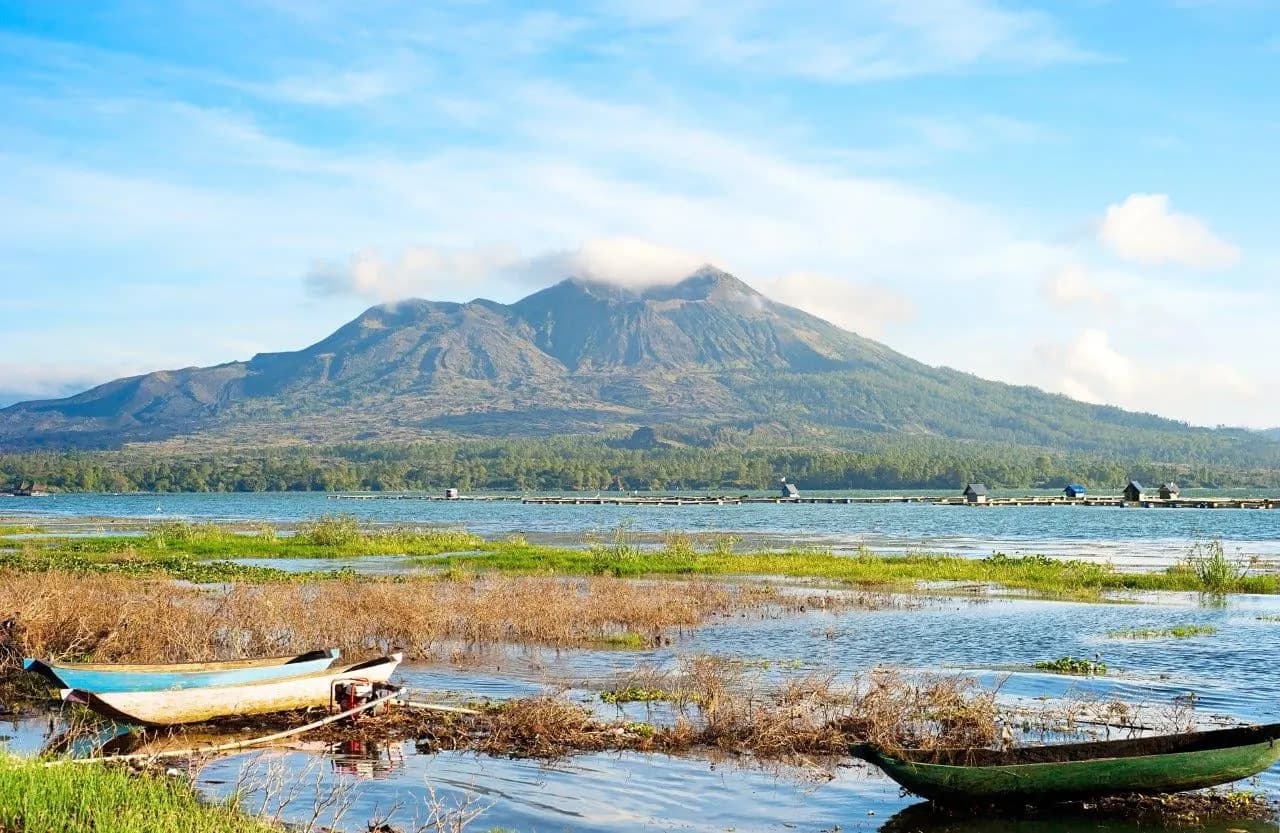 Mount Batur above the lake with wooden canoes pulled up on the shore