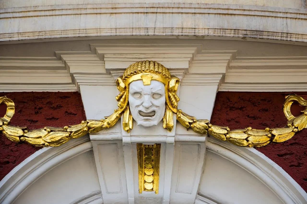 A gilded theatre mask and garland above an arched doorway
