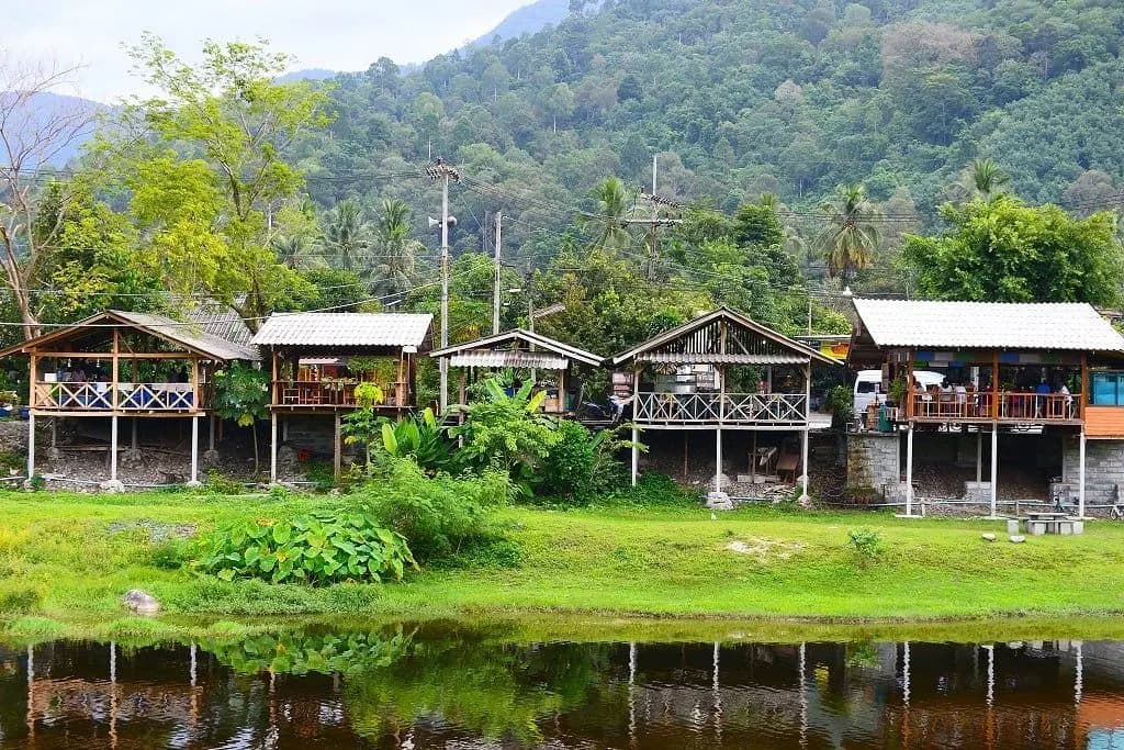 Wooden stilt houses beside a stream below forested hills
