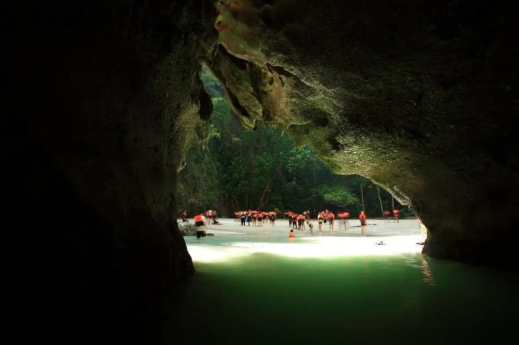 Swimmers at the mouth of a sea cave opening onto green water