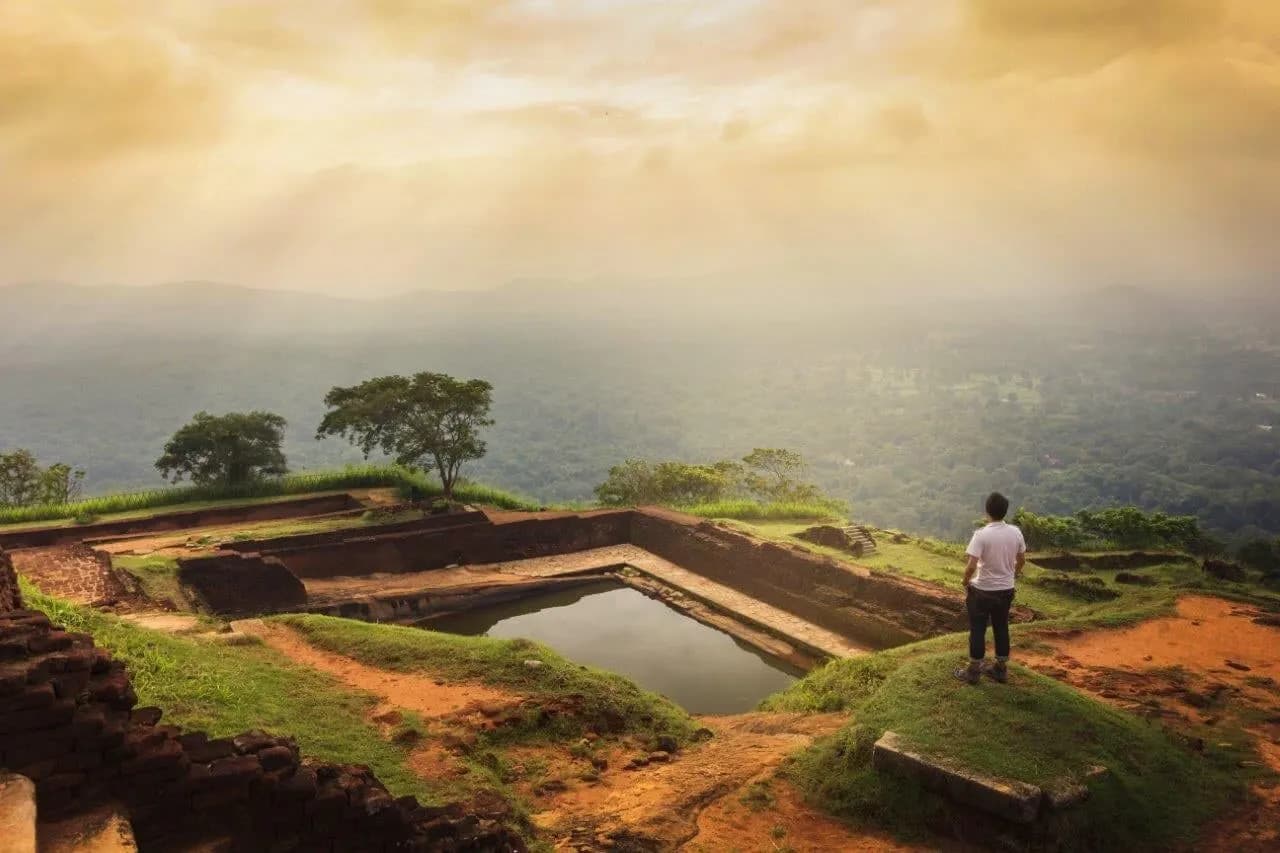 A traveller standing by the ancient pool on the summit of Sigiriya at sunrise