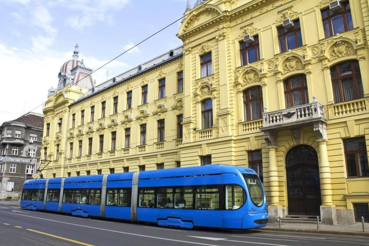 A blue tram passing an ornate yellow building in Zagreb